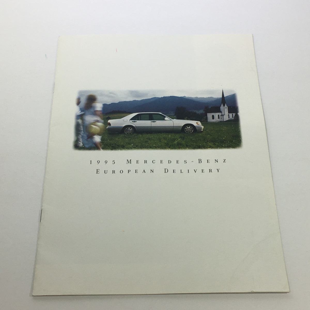 Cover of the 1995 Mercedes-Benz European Delivery Dealership Car Auto Brochure Catalog featuring a silver Mercedes-Benz car parked in a picturesque landscape with mountains and a church.