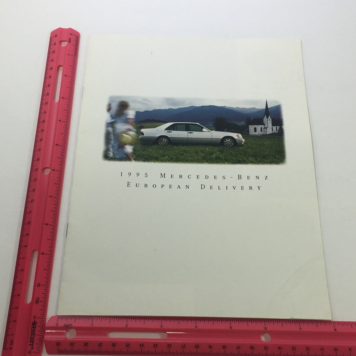 1995 Mercedes-Benz European Delivery Dealership Car Auto Brochure Catalog cover featuring a sleek white Mercedes-Benz with a countryside backdrop, including a child playing with a ball and a church in the distance.