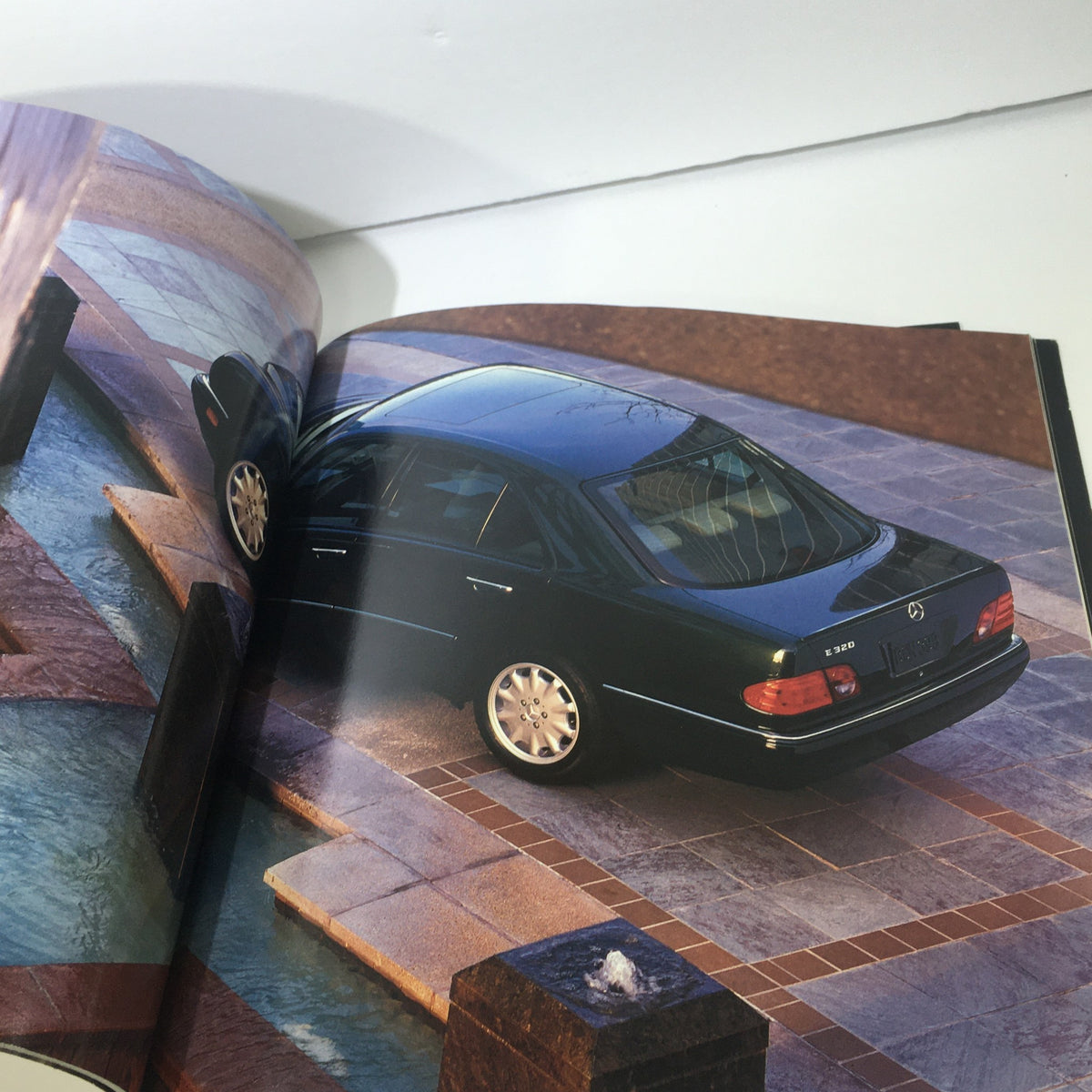 Exterior shot of the 1997 Mercedes-Benz E-Class parked by a fountain in the dealership car brochure.
