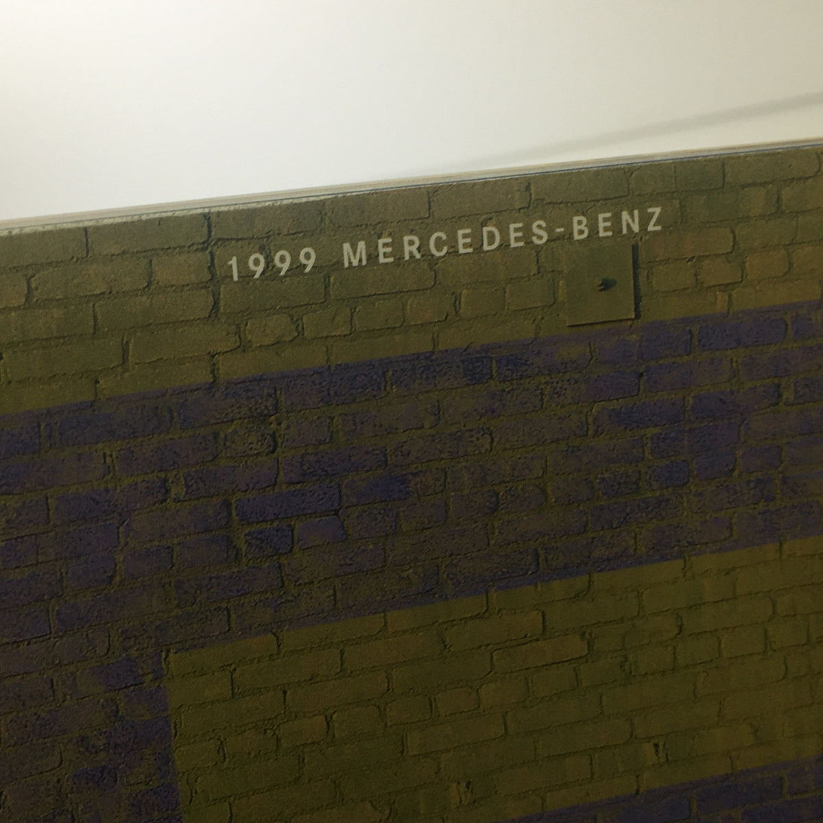 Detailed view of the top edge of the 1999 Mercedes-Benz E-Class Dealership Car Auto Brochure Catalog displaying '1999 MERCEDES-BENZ' on a textured brick background.