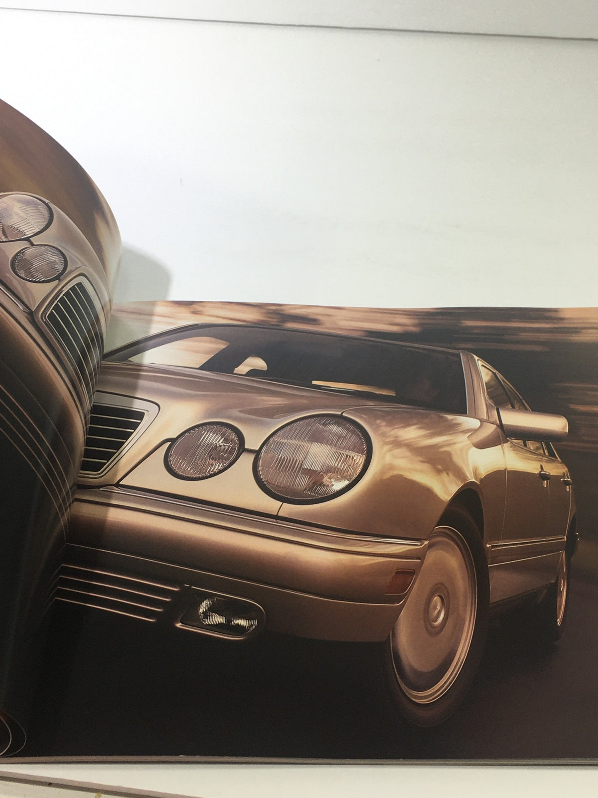 Interior view of the 1999 Mercedes-Benz E-Class Dealership Car Auto Brochure Catalog displaying a bronze-colored Mercedes-Benz E-Class in motion.