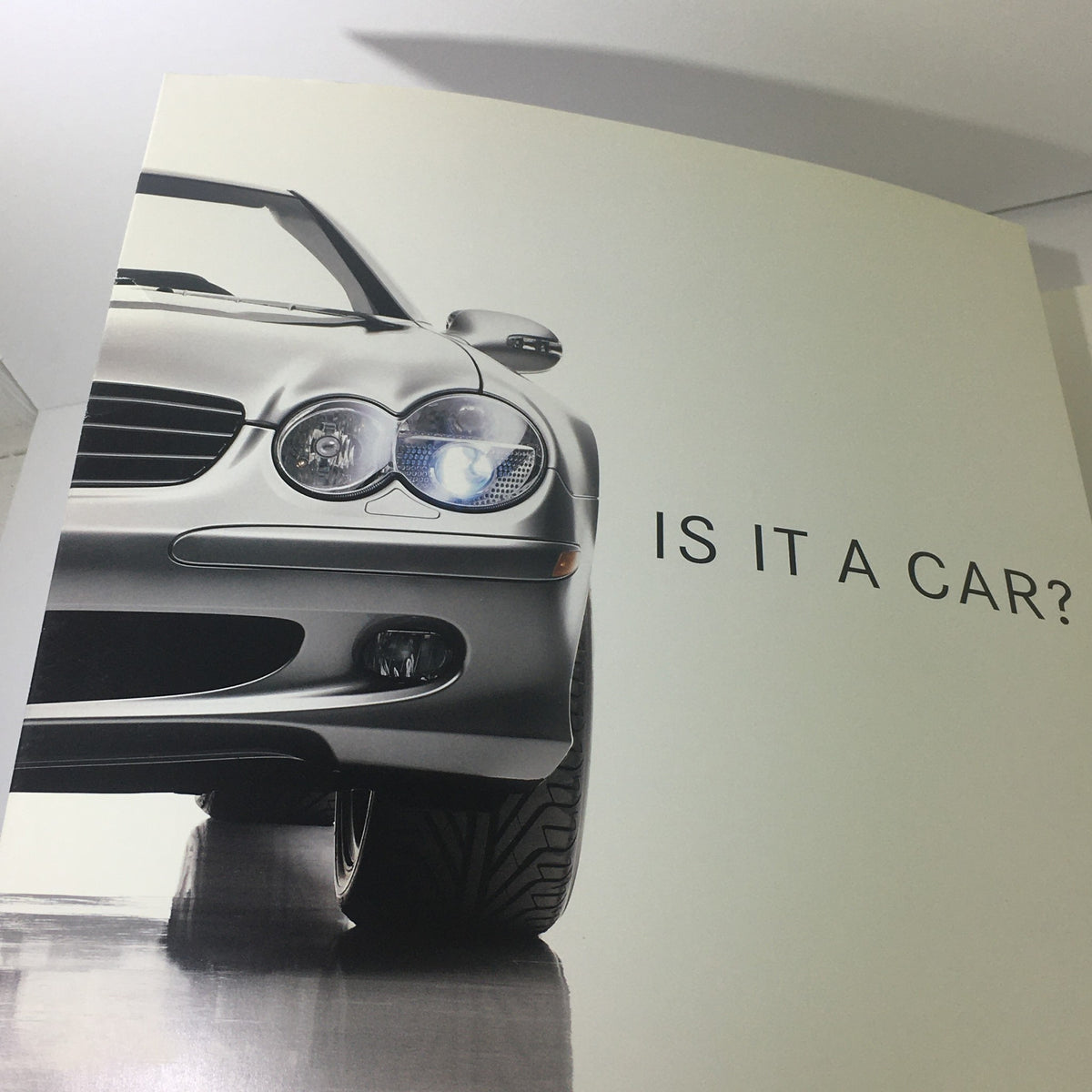 Artistic image showing the front of the silver SL-Class with the text 'IS IT A CAR?' from the 2003 Mercedes-Benz 5th Generation SL-Class Dealership Car Auto Brochure Catalog.