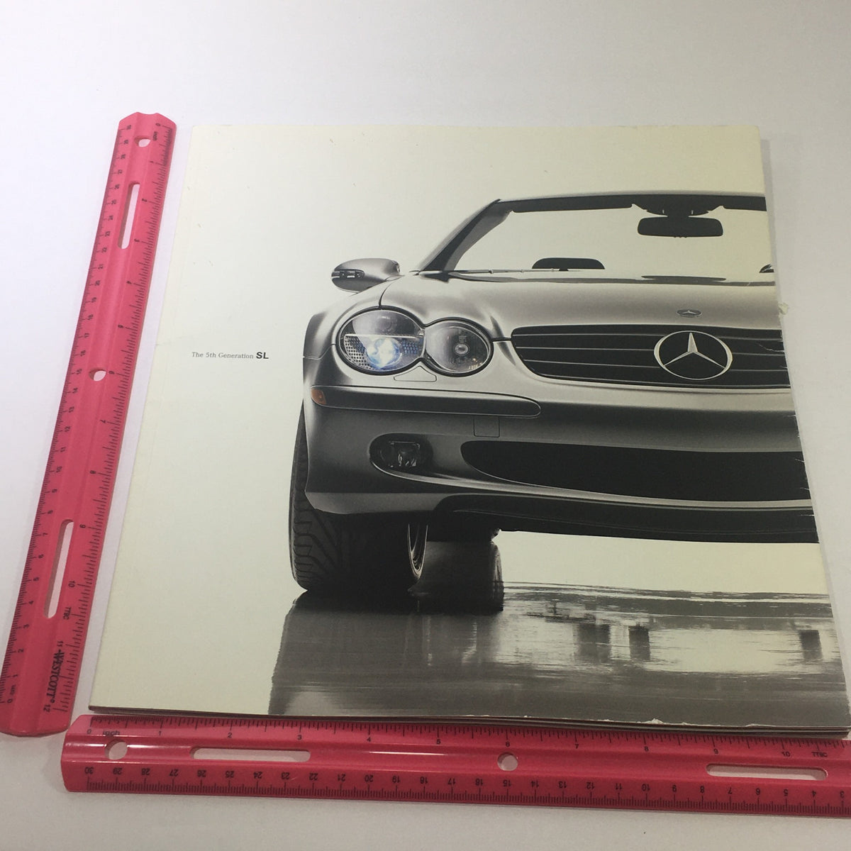 Front cover photo of the 2003 Mercedes-Benz 5th Generation SL-Class Dealership Car Auto Brochure Catalog featuring the sleek design of the car, with a ruler for size comparison.