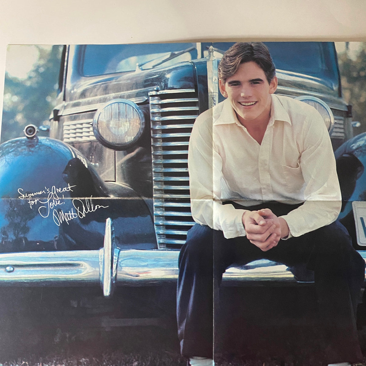 A vintage photo of Matt Dillon smiling and sitting on the hood of an antique car, featured in Teen Beat Magazine October 1980. This classic image captures the charm of teen idols from the era.