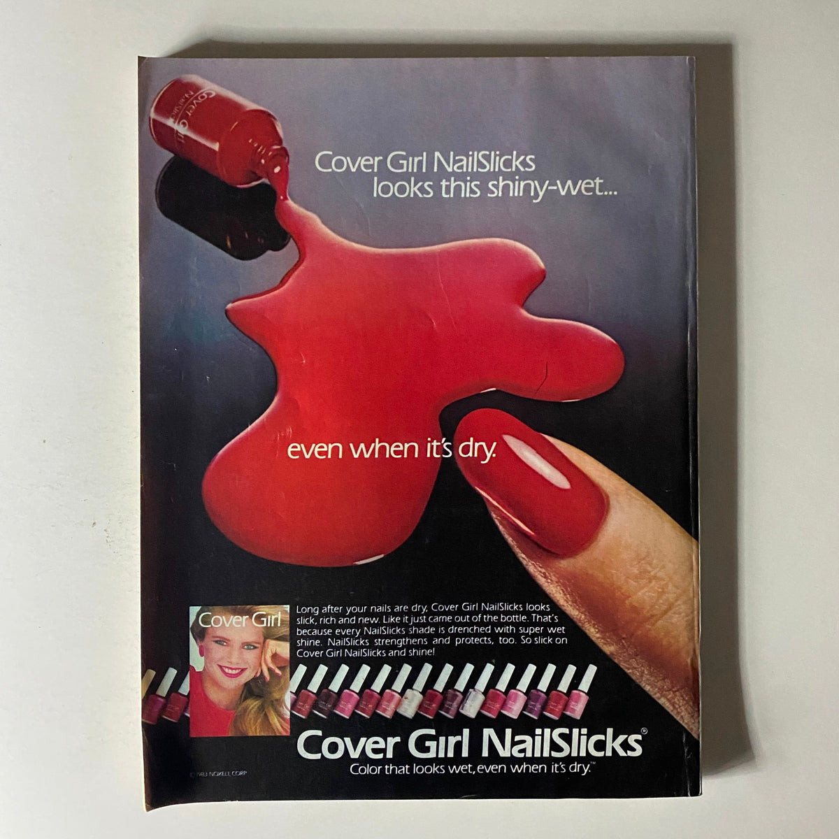 Cover Girl NailSlicks advertisement featuring vibrant red nail polish dripping on a surface, highlighting its shiny, wet appearance even when dry, alongside the slogan as seen in the Glamour Magazine July 1983 issue.