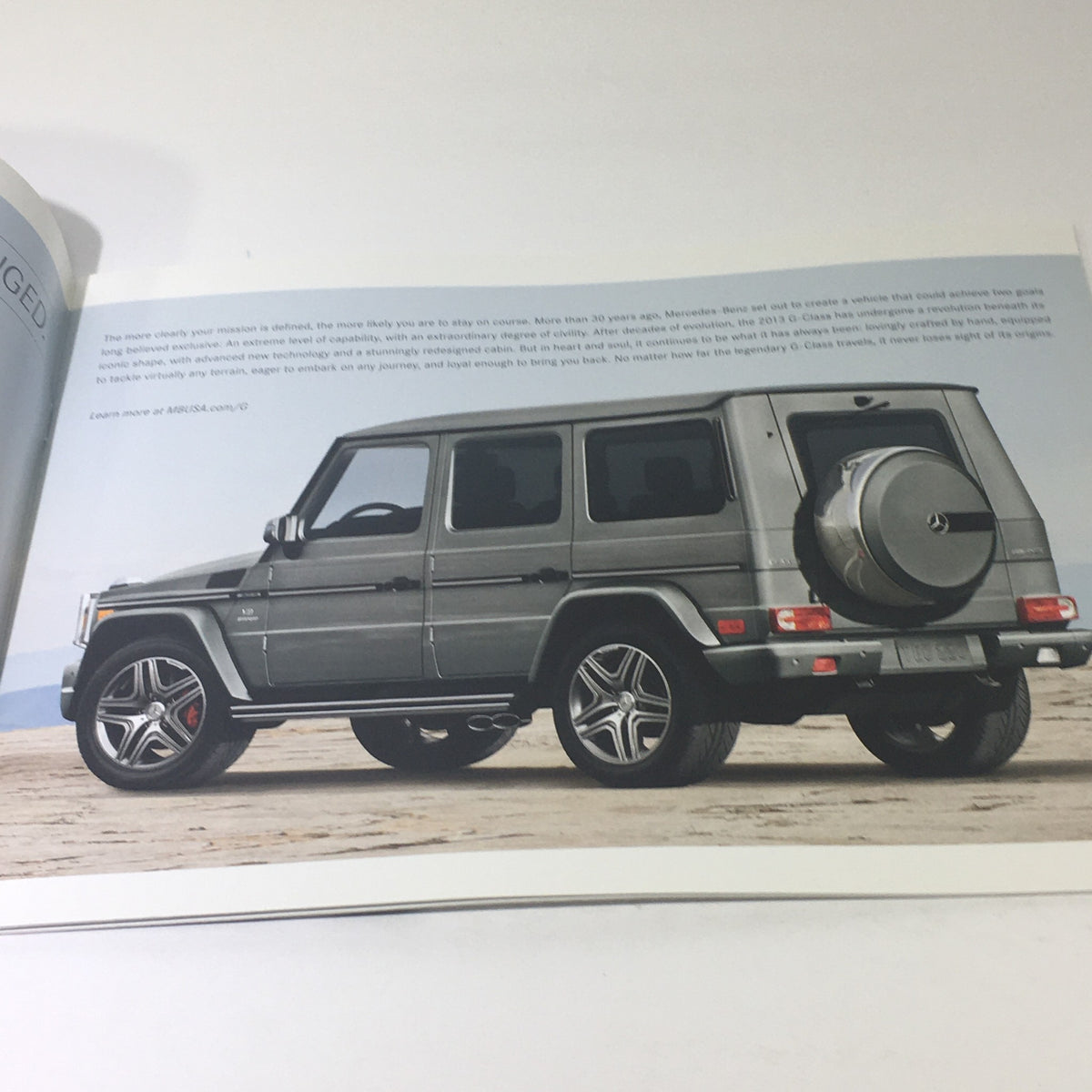 Page from the 2013 Mercedes-Benz G-Class 4x4 AMG brochure displaying a side view of the vehicle on a scenic backdrop, emphasizing its powerful stance.