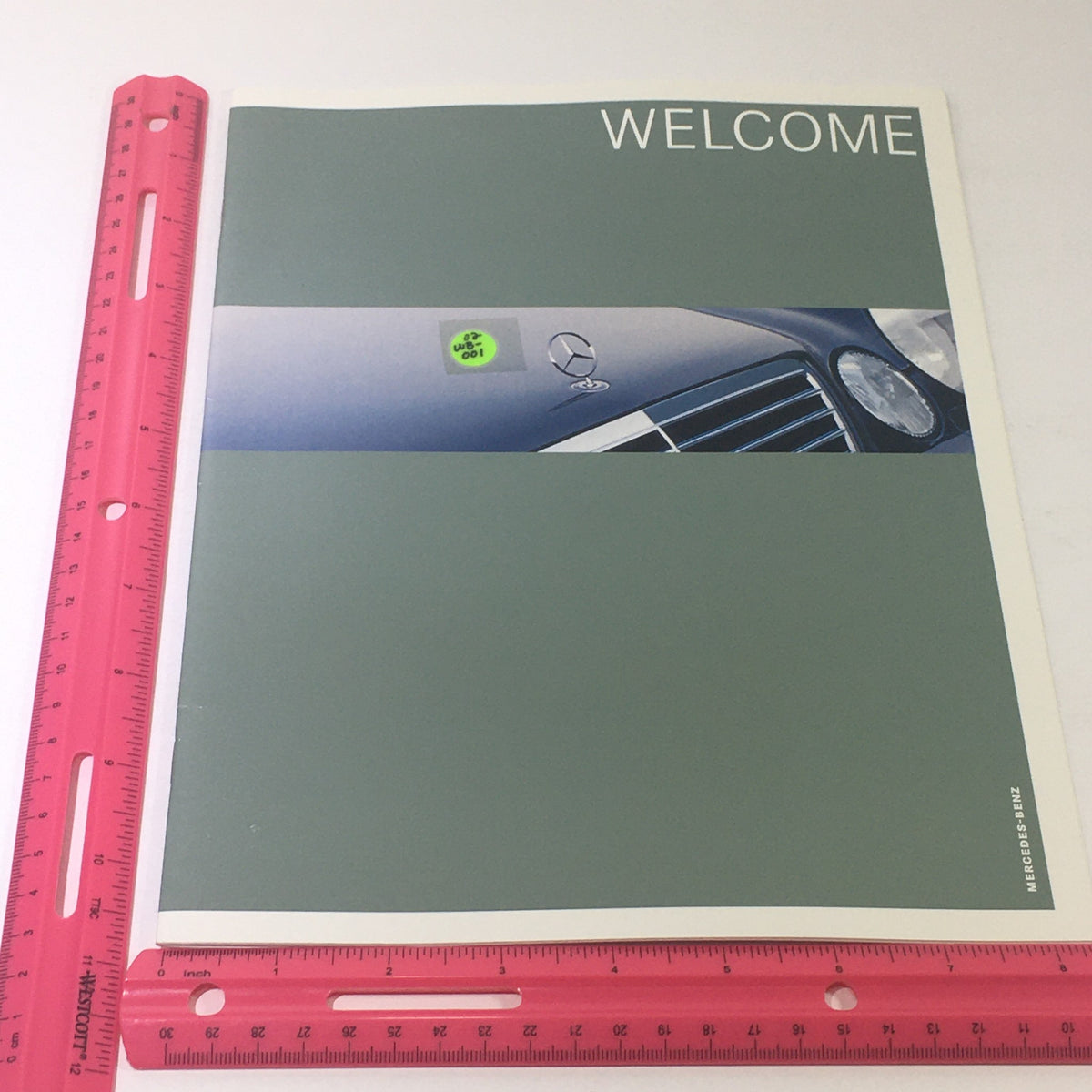 Front cover of the 2001 Mercedes-Benz E-Class Dealership Car Auto Brochure Catalog, showing a close-up of the car's grille and the word 'WELCOME', complemented by a pink ruler for size reference.