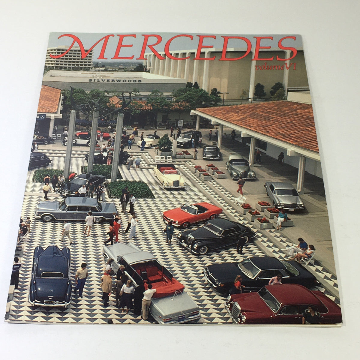 Cover of the 1982 Mercedes-Benz Volume VI Dealership Car Auto Brochure Catalog featuring an aerial view of a vibrant car dealership showcasing classic Mercedes-Benz cars with people interacting in an outdoor setting.