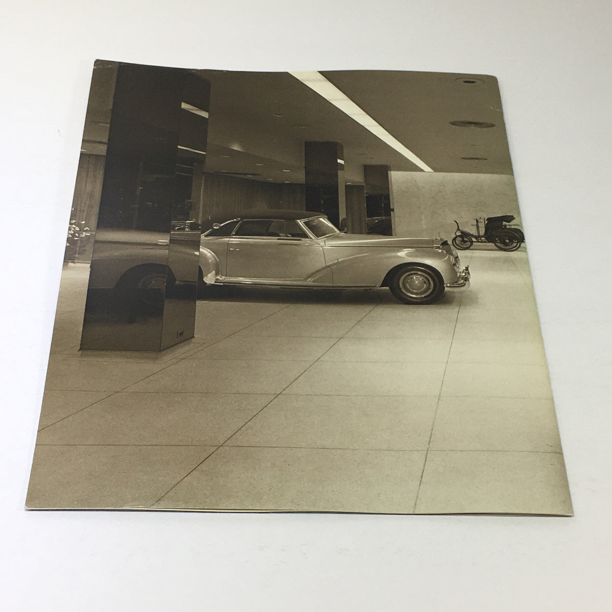 Black and white image from the 1983 Mercedes-Benz Volume VIII Dealership Car Auto Brochure, showcasing a classic Mercedes-Benz car in a modern dealership setting.