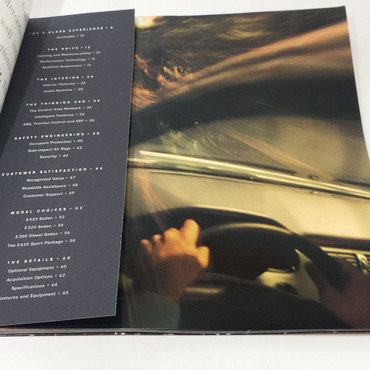 Close-up view of hands on the steering wheel from the 1997 Mercedes-Benz E Class Coupe dealership car auto brochure catalog, showcasing driving experience and interior features.