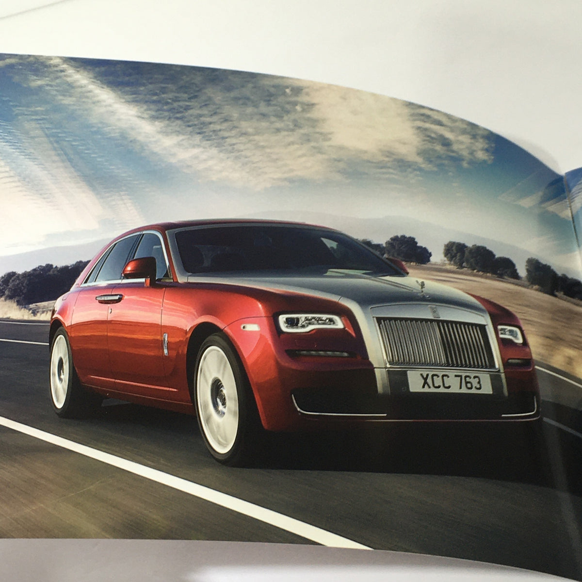 Stylish 2014 Rolls Royce Ghost Family Dealership Car Auto Brochure Catalog image of a sleek Rolls Royce car driving on a scenic road.