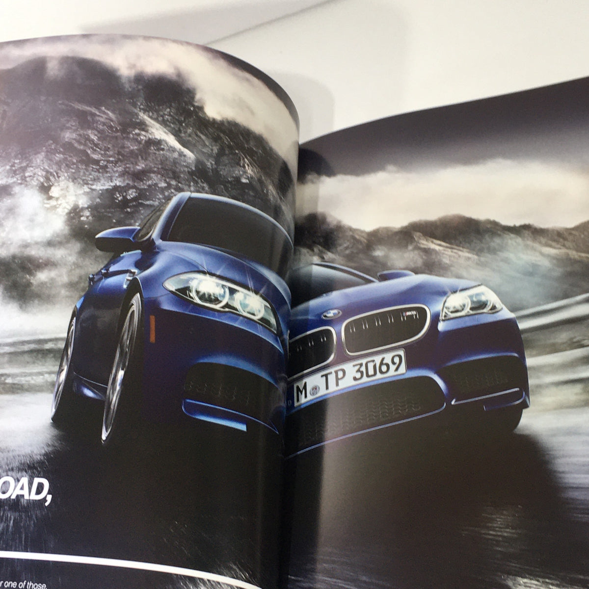 Interior page of the 2014 BMW M5 Dealership Car Auto Brochure Catalog displaying a blue BMW M5 on a scenic road, emphasizing its performance features.