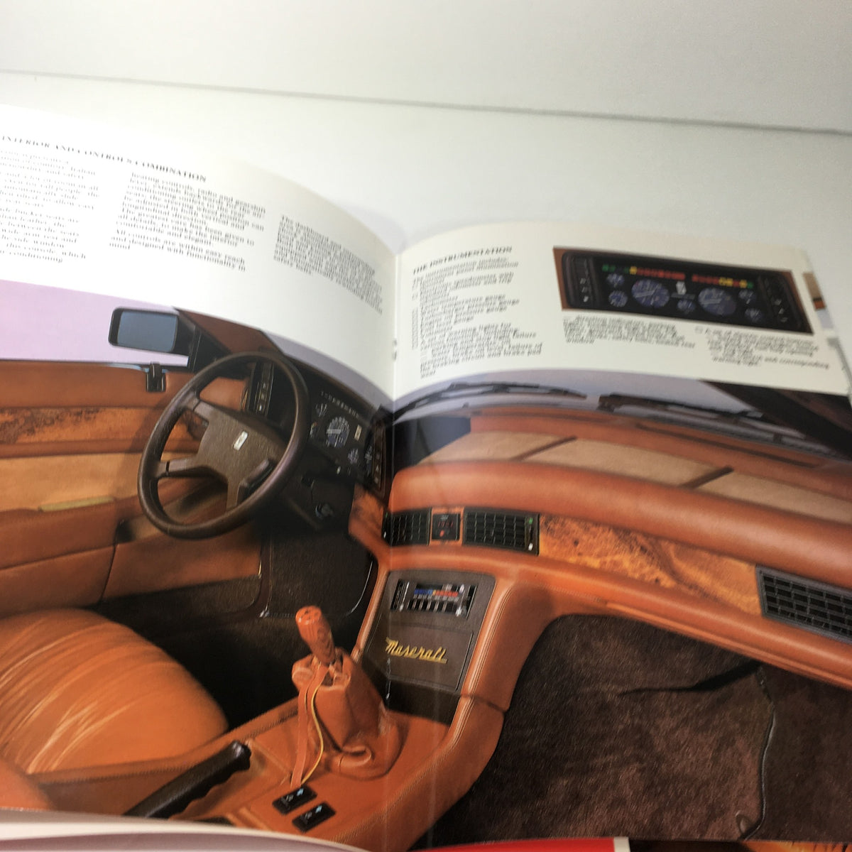 Interior view of the 1985 Maserati Biturbo as depicted in the dealership car auto brochure catalog, showcasing the dashboard and seat design.
