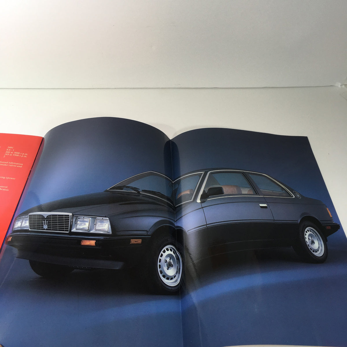 1985 Maserati Biturbo Dealership Car Auto Brochure Catalog featuring a glossy image of the Maserati Biturbo against a blue background.