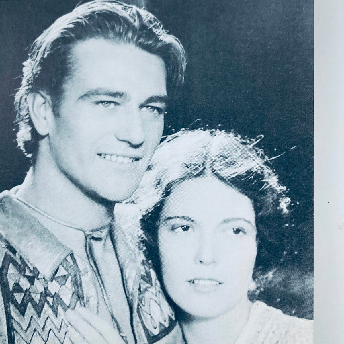Image of a vintage black and white photograph featuring two actors, a male and female, smiling closely together, from the VTG 1976 The Films of John Wayne by Mark Ricci, Boris & Steve Zmijewsky.