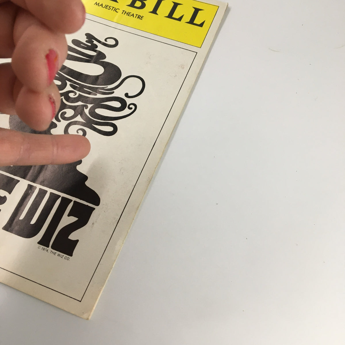 Close-up of the 1975 Playbill for The Wiz showing a hand lightly touching the cover design featuring flowing hair and silhouette.
