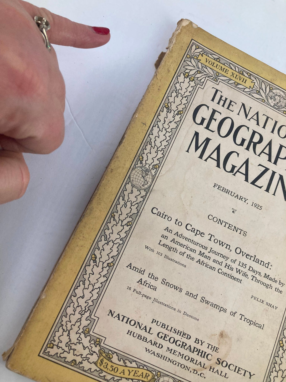 Detailed view of the vintage National Geographic Magazine - February 1925 cover, highlighting minor wear and a finger pointing at the content section, emphasizing its collectible nature.