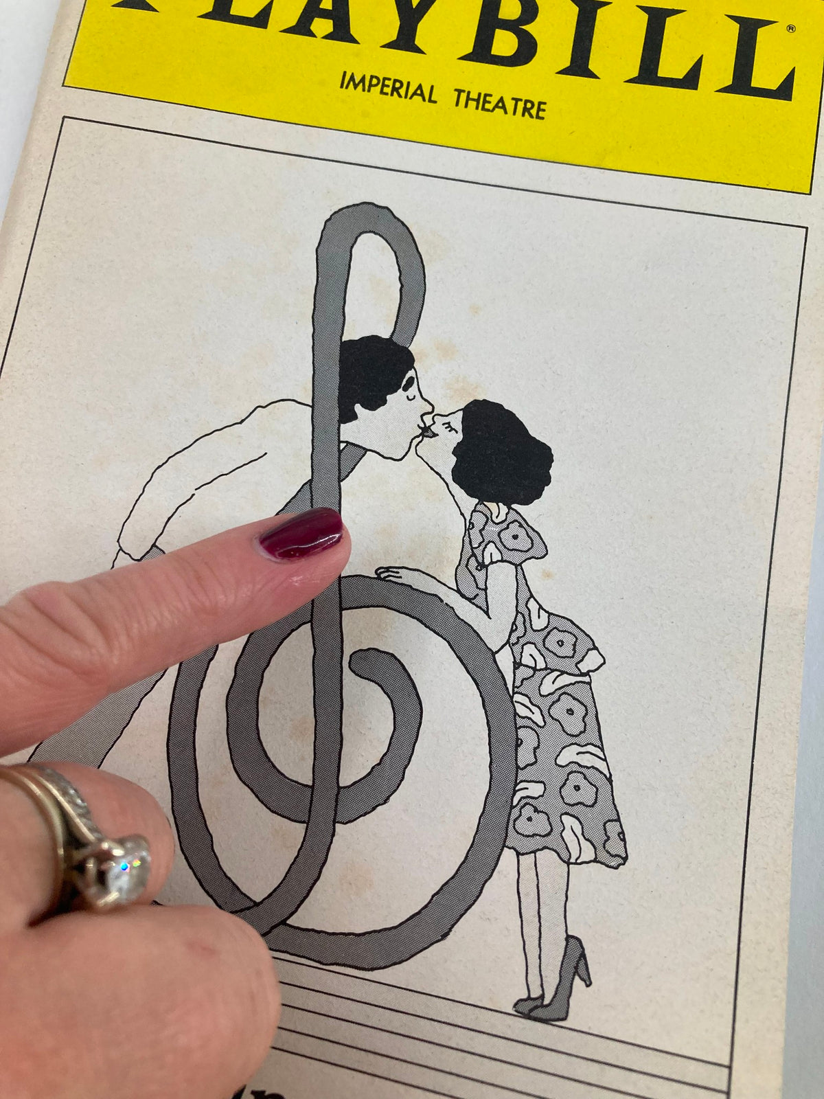 Close-up of the 1980 'They're Playing Our Song' Playbill showing a woman pointing at a treble clef illustration amid a kiss.