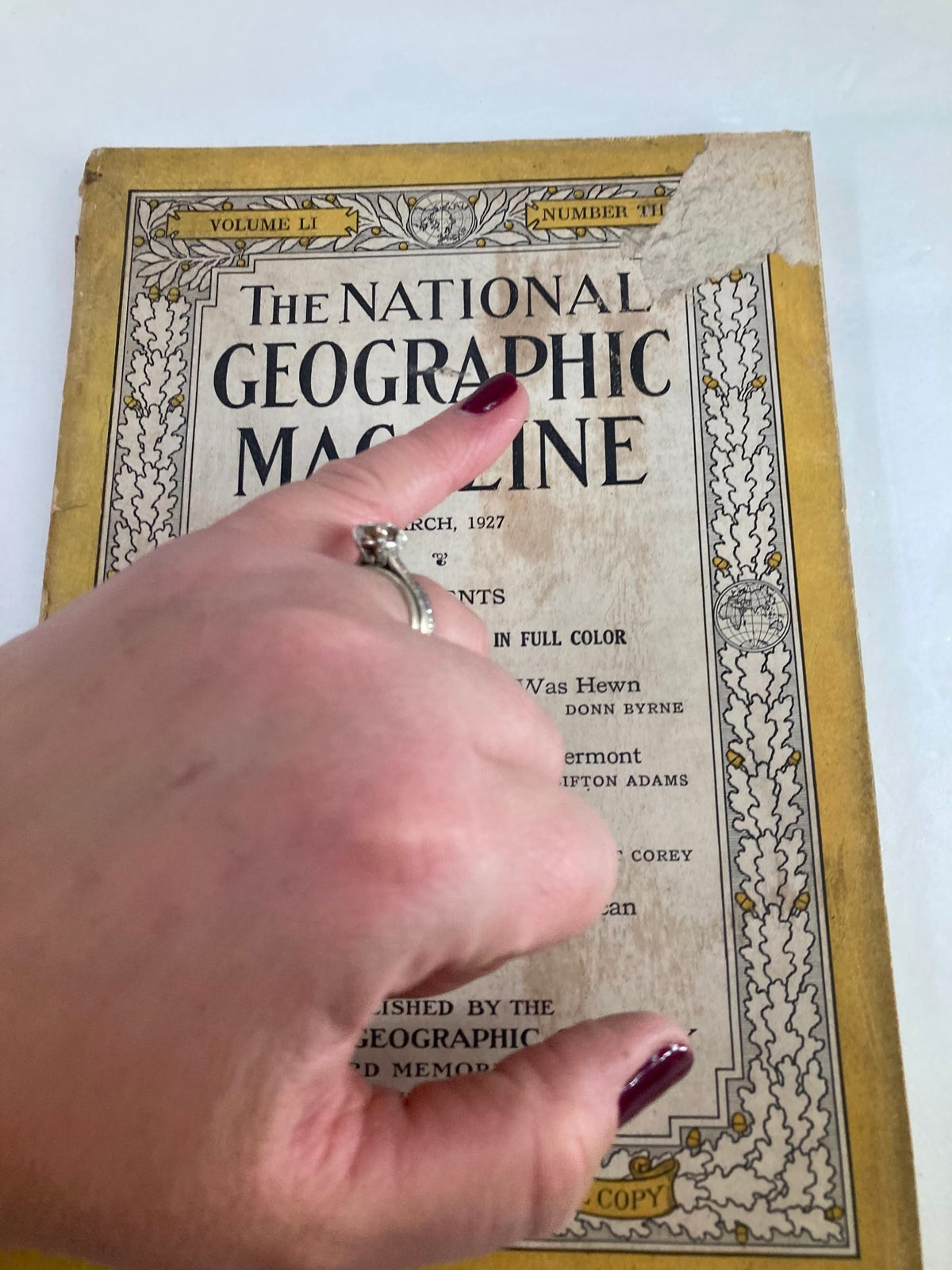 Close-up view of the cover of VTG The National Geographic Magazine March 1927, showing wear and a tear, along with a hand pointing at the title.