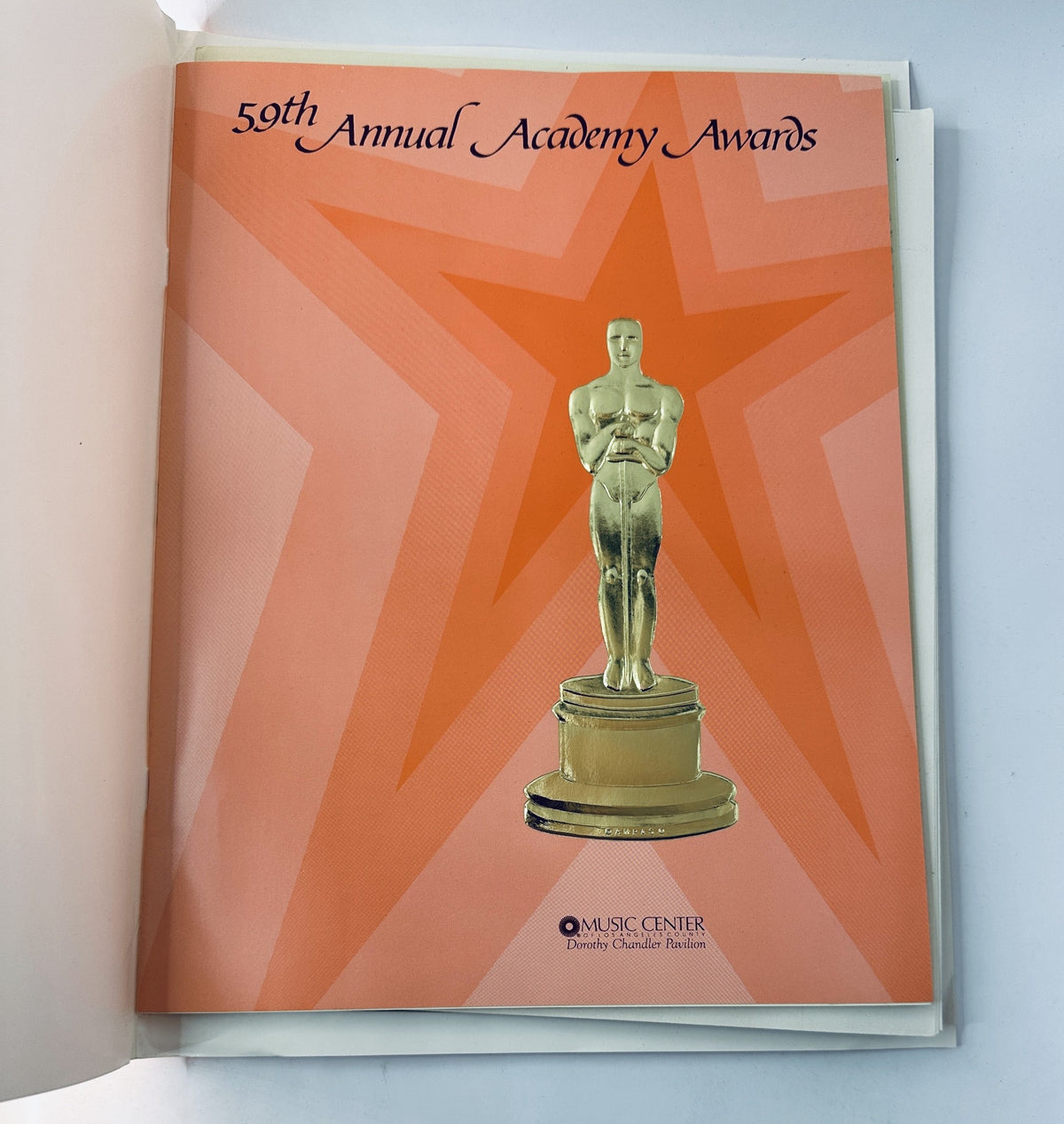 Interior page of the Oscars Night Magazine for the 59th Annual Academy Awards, showcasing a golden Oscar statuette on an orange star background.