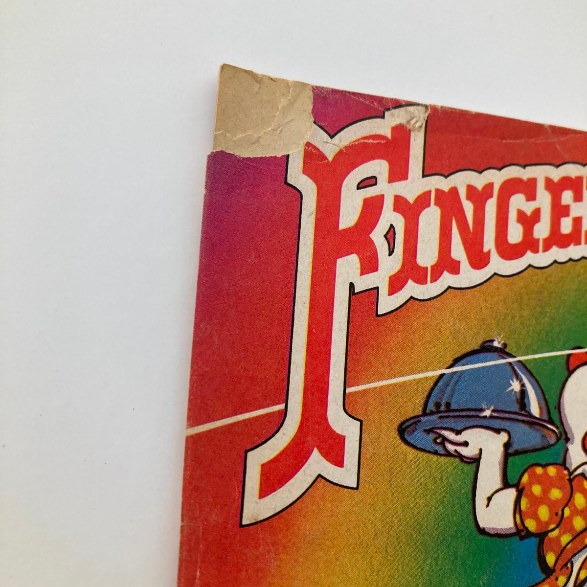 Close-up of the corner damage on the cover of Finger Pickin' Good magazine, illustrating its vintage condition while retaining its appeal as a collectible item for music magazine connoisseurs.