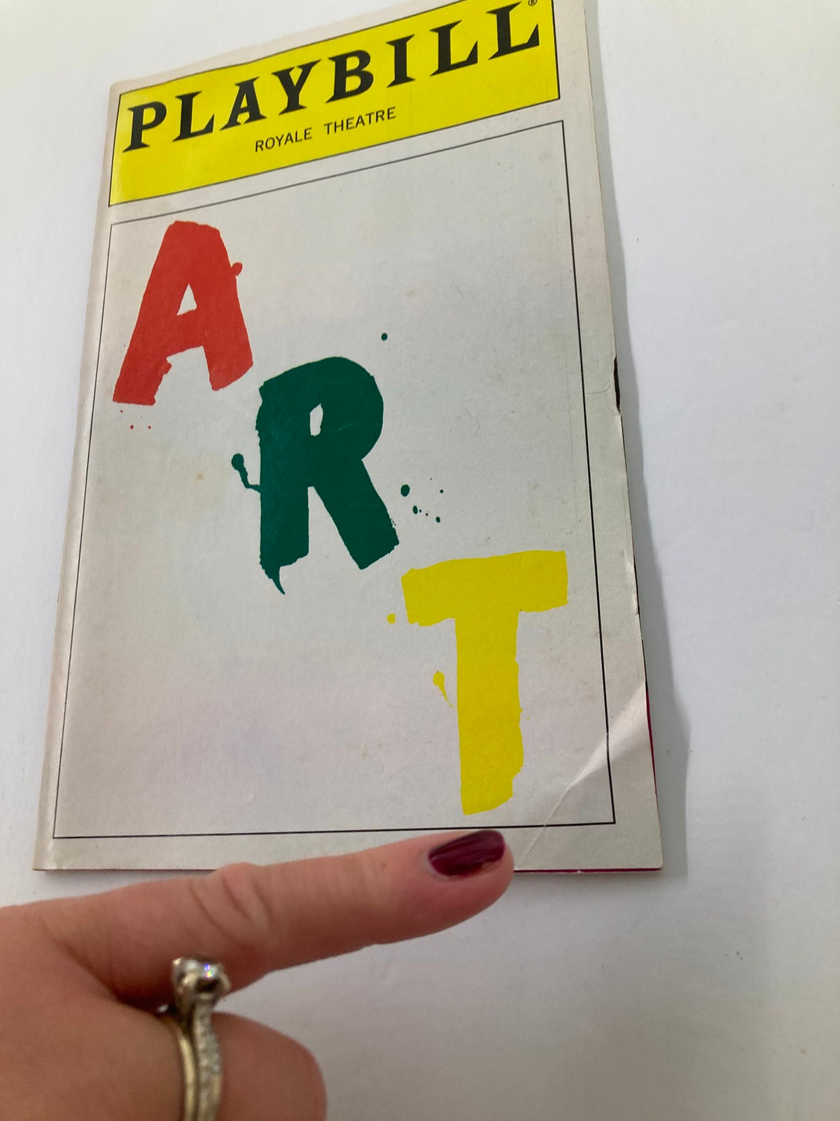 Close-up of the 1998 Playbill from the Royale Theatre for 'Art,' with a finger pointing at the cover’s colorful title, highlighting its vintage appeal.