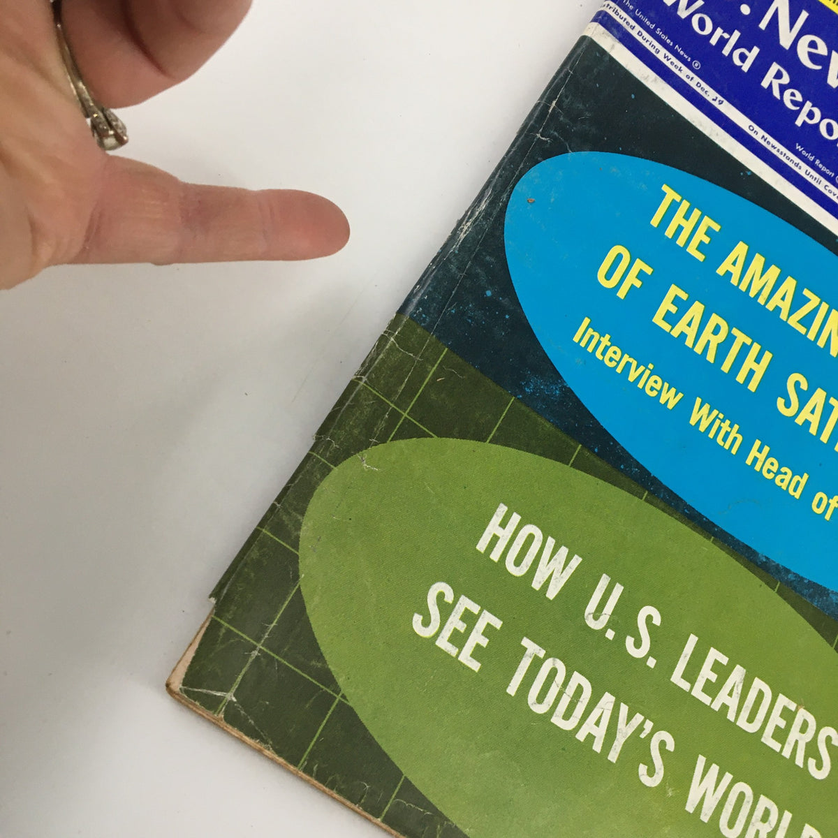Close-up of the cover of US News & World Report Magazine, December 26, 1966, highlighting 'The Amazing Story of Earth Satellites' with a hand pointing to it.