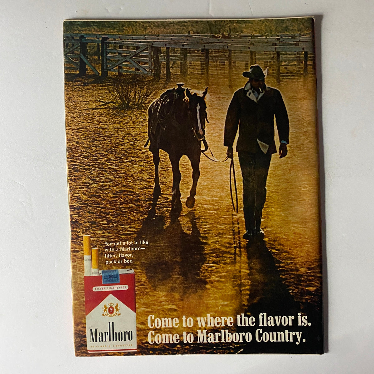 Vintage Marlboro advertisement featuring a cowboy walking a horse in Marlboro Country, promoting the brand's filter cigarettes with a scenic background.