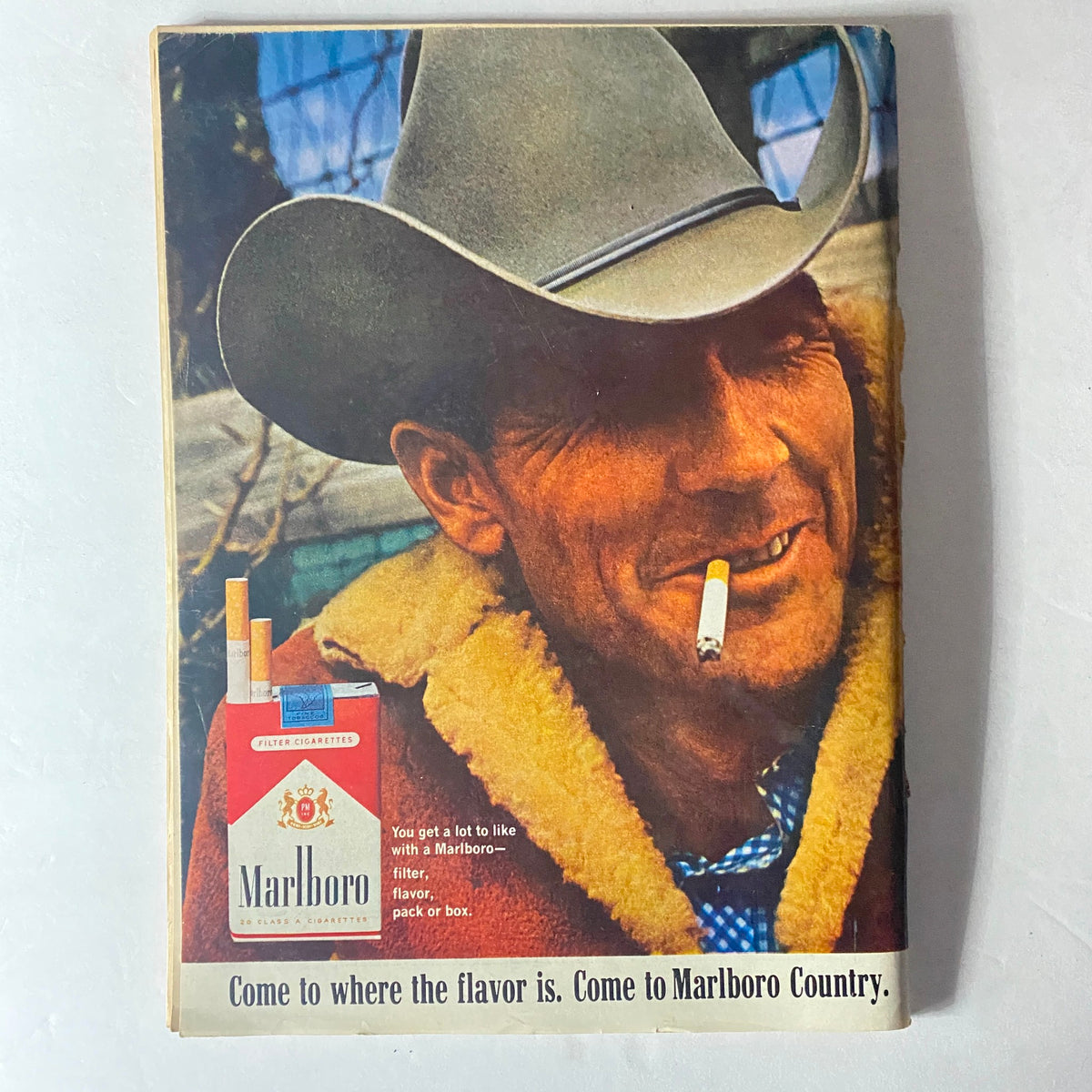 Vintage advertisement for Marlboro cigarettes showcasing a cowboy with a cigarette, promoting the slogan 'Come to where the flavor is. Come to Marlboro Country.'