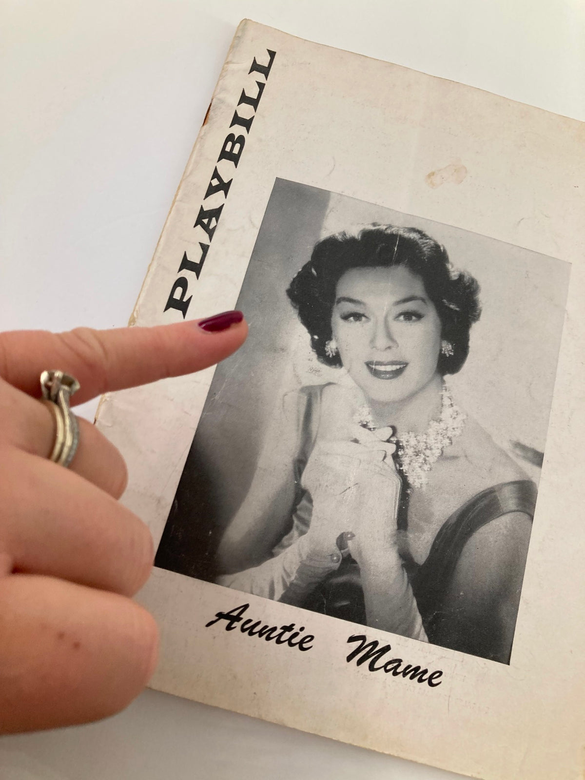 Close-up of the 1957 Playbill for Auntie Mame, featuring a hand pointing at Rosalind Russell's image, highlighting the collectible nature of the magazine.