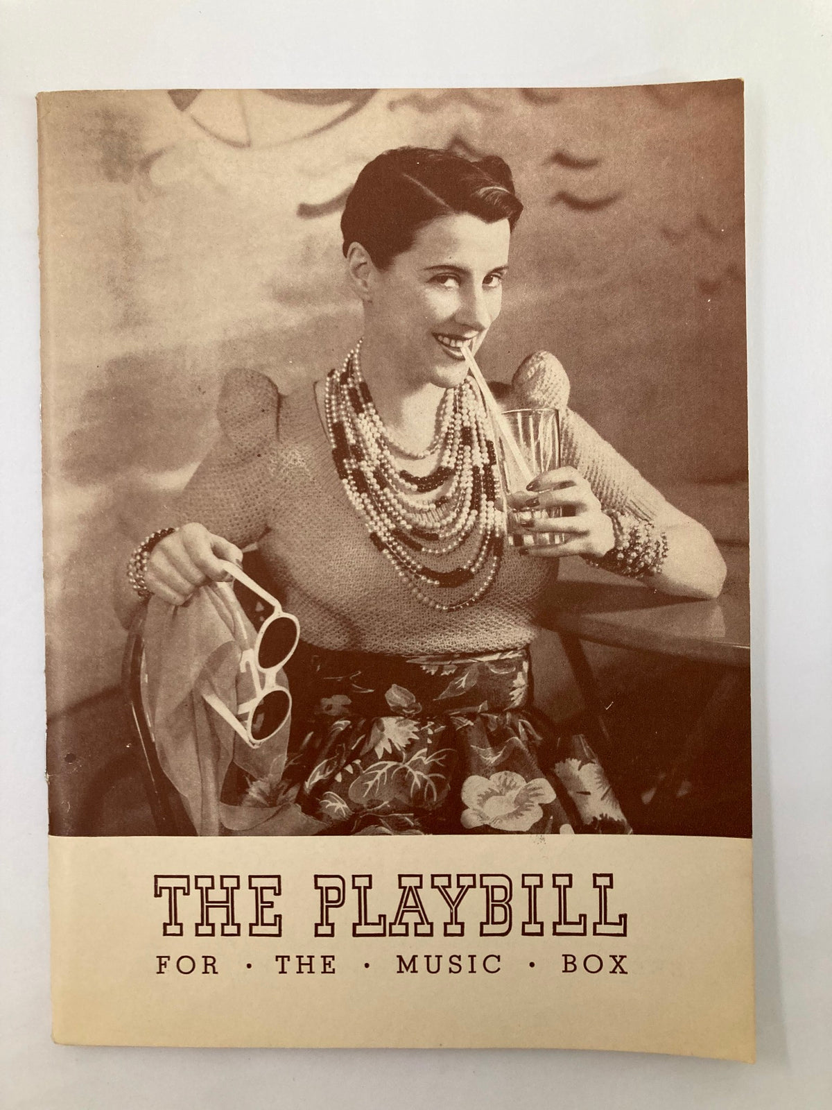 1939 Playbill for The Music Box featuring a vintage photograph of a woman enjoying a beverage, adorned with pearl necklaces and stylish sunglasses.