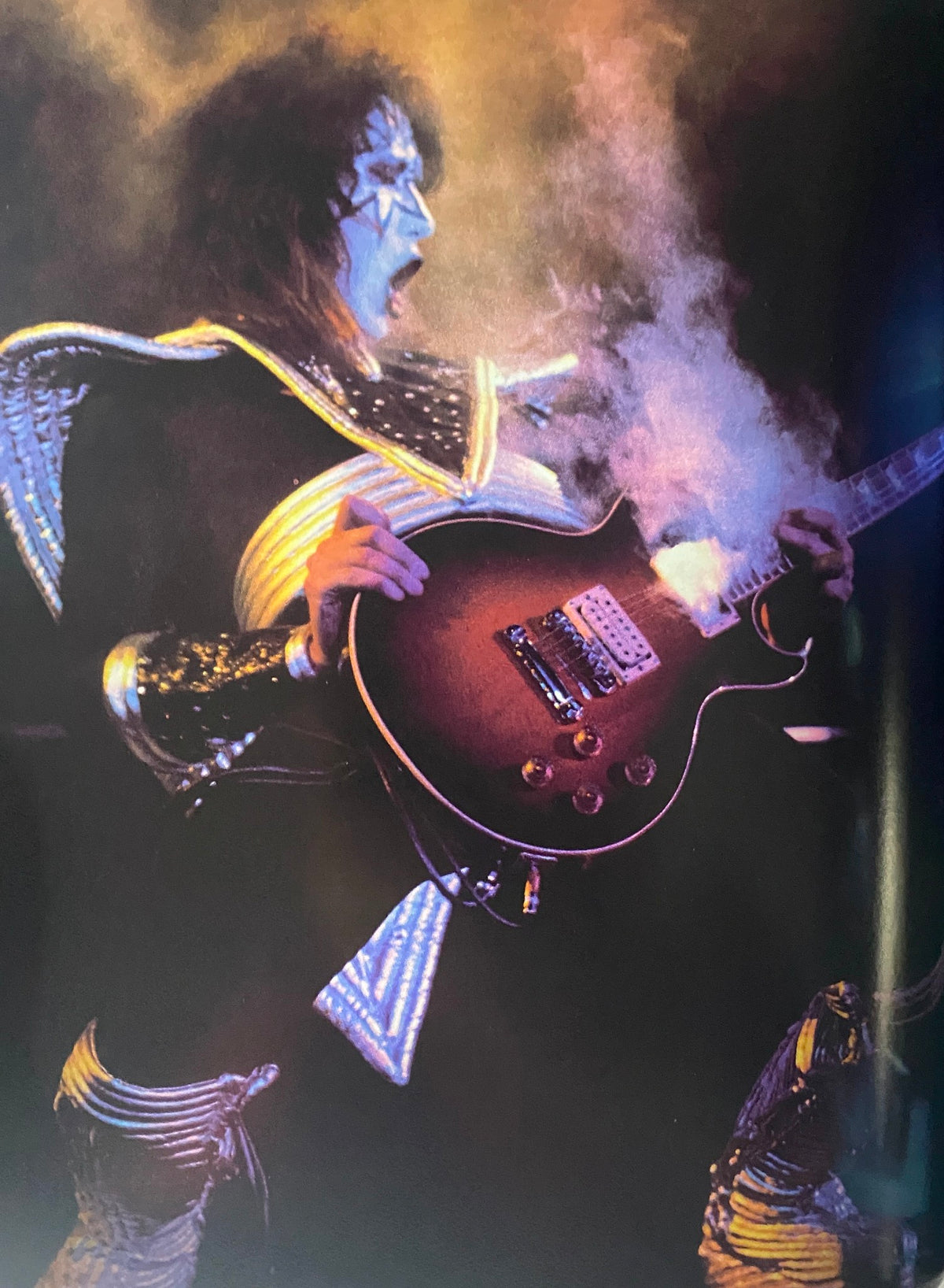 Dynamic performance photo from 'The KISS Years' by Barry Levine, featuring a band member in a sparkling costume playing the guitar with dramatic lighting and smoke effects.