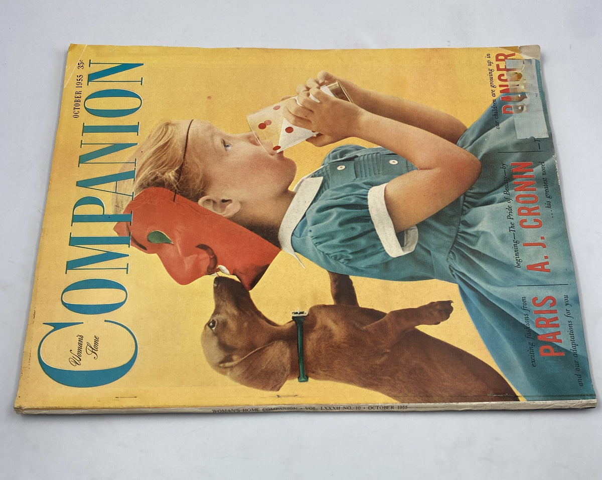 Front cover of Woman’s Home Companion Magazine October 1955 displaying a girl sipping a drink with a dog playfully interacting, themed around Paris fashions and the works of A. J. Cronin.