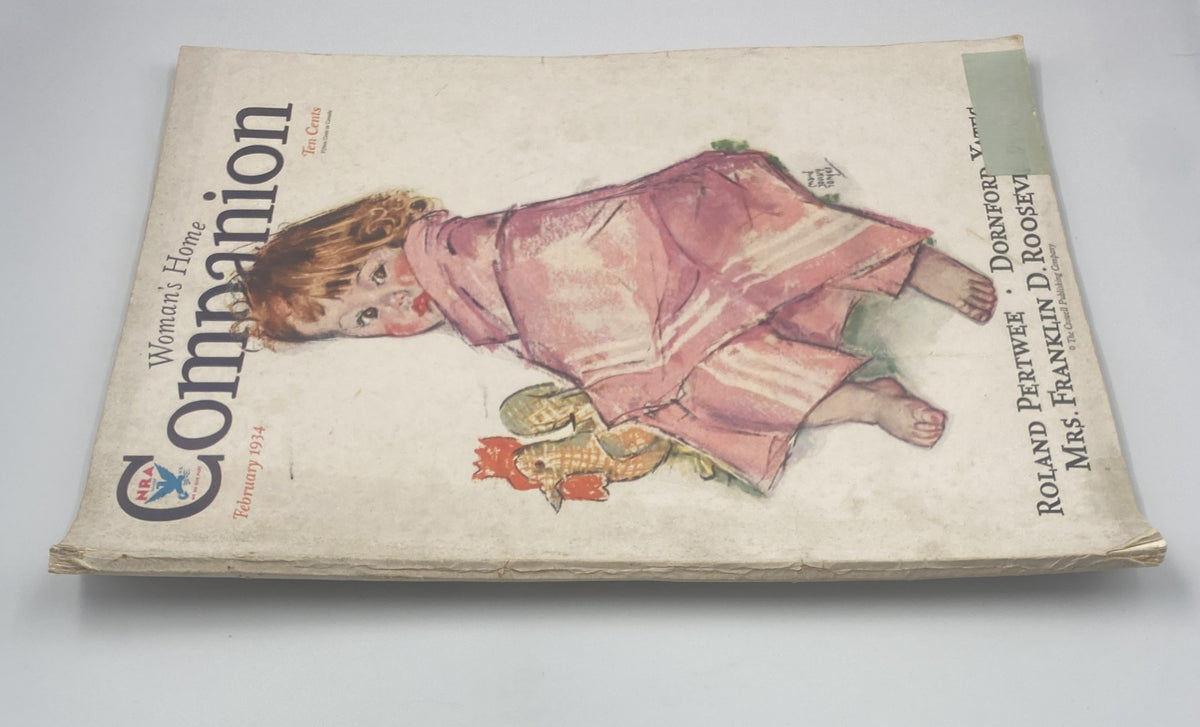 Side view of Woman’s Home Companion Magazine February 1934, illustrating the spine and front cover with an image of a young girl holding a toy, highlighting the publication's vintage charm.