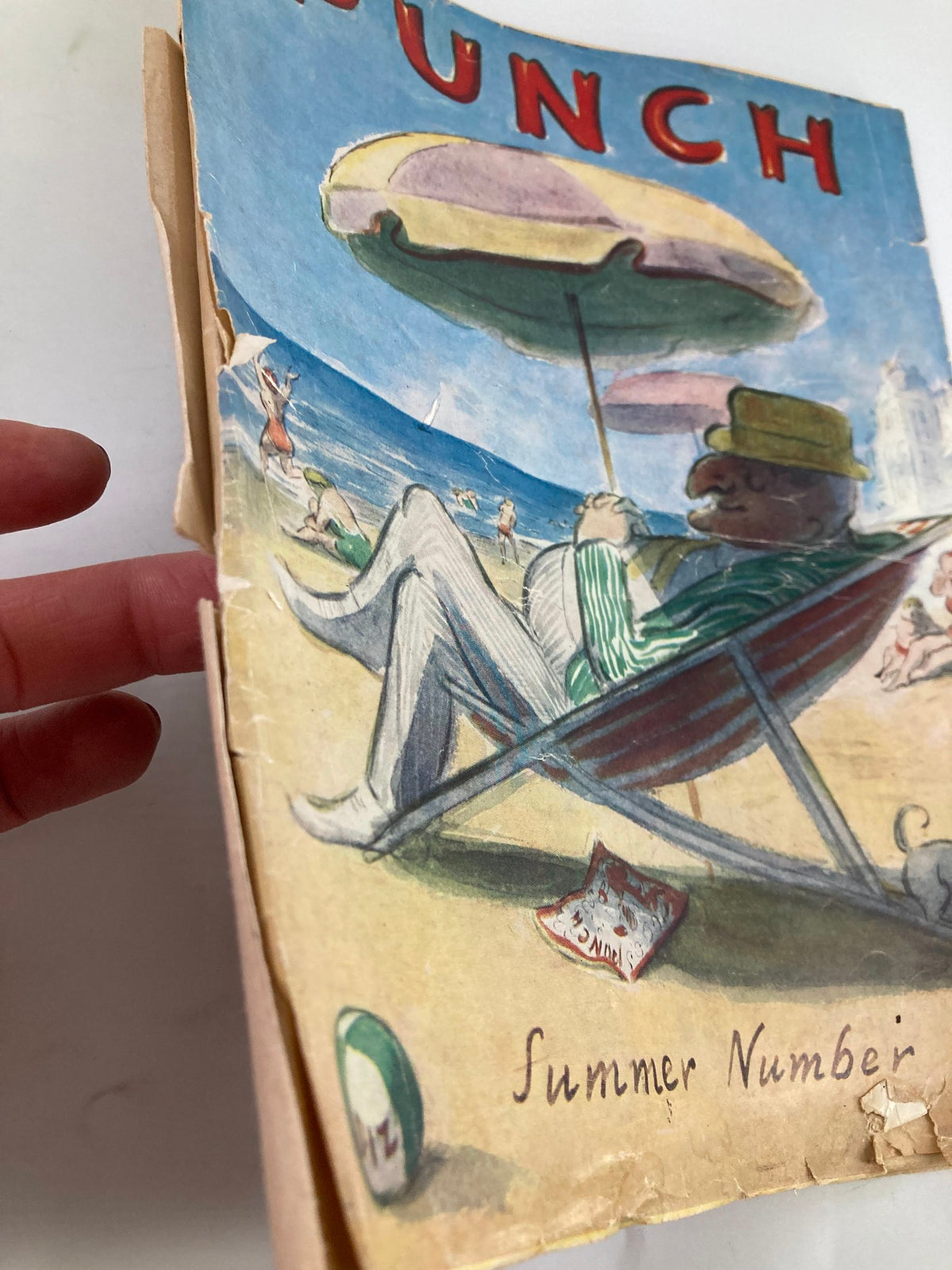 Side view of the VTG Punch Magazine May 25 1955 Summer Number, displaying the magazine's cover and wear over time, featuring the playful beach scene and colorful graphics.