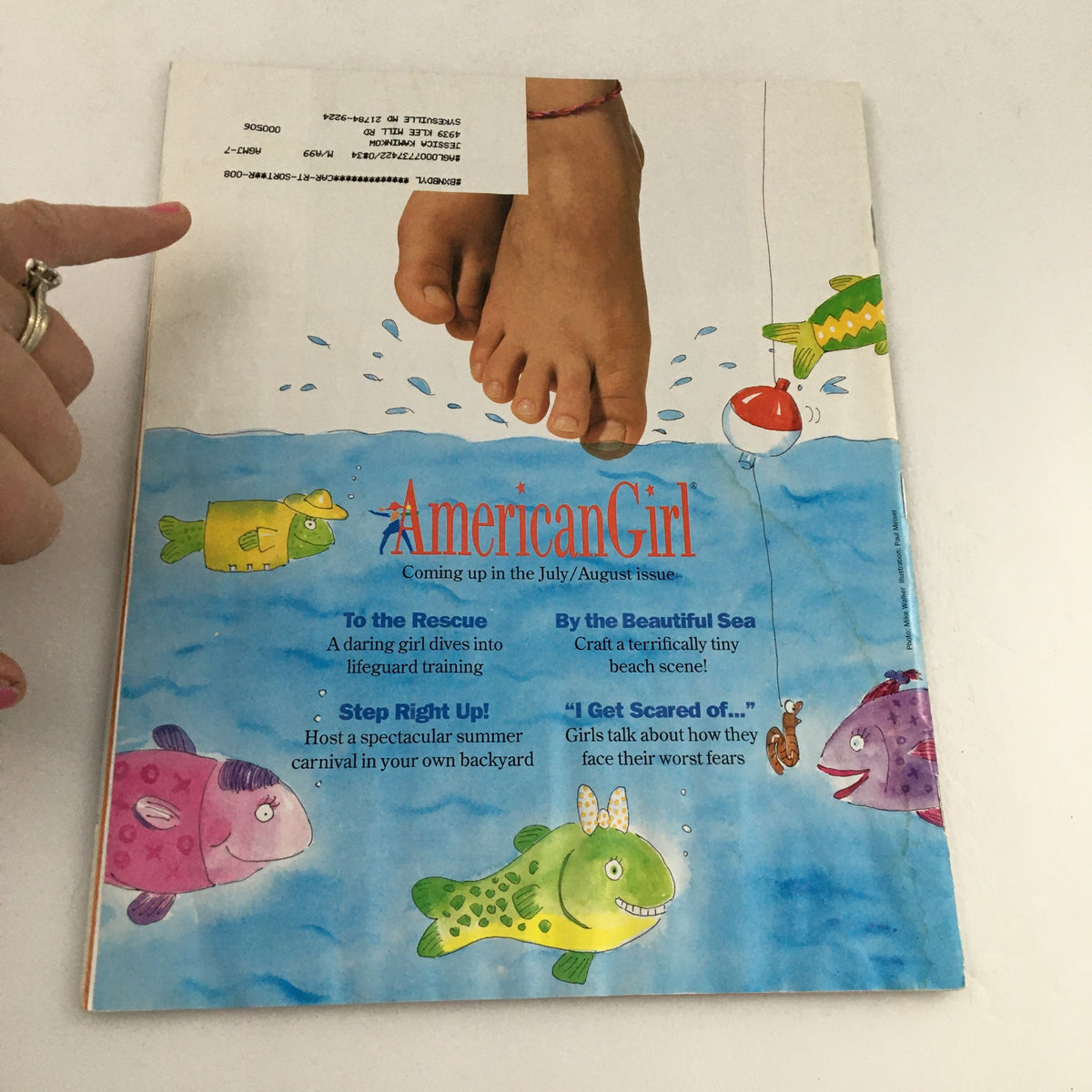 Back cover of American Girl Magazine May-June 1998 with a colorful illustrated scene of fish and a girl's feet, promoting the upcoming July-August issue.