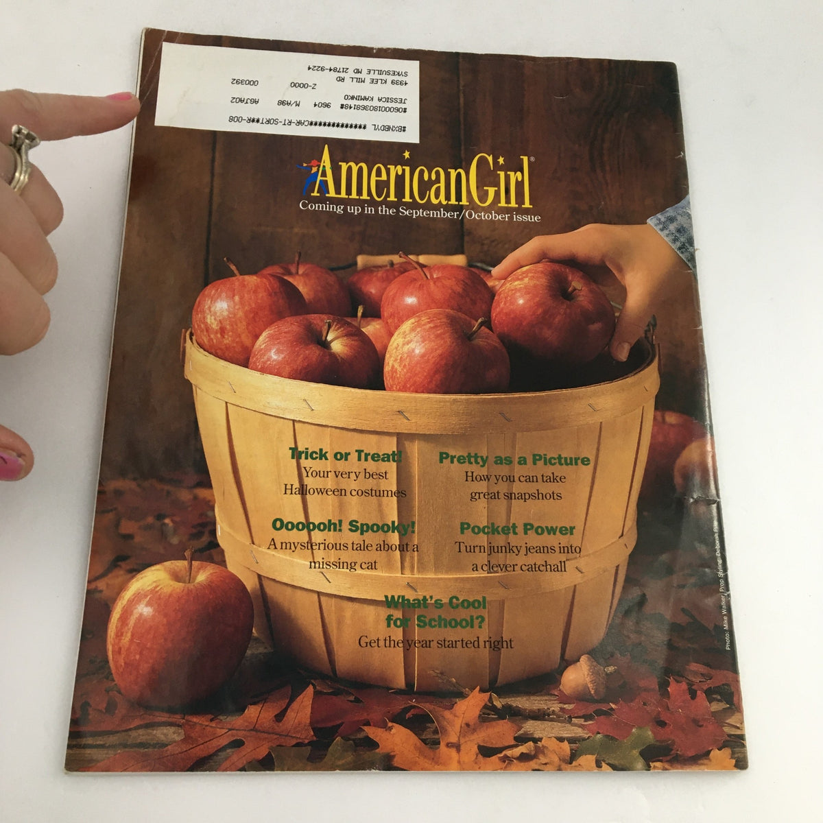 Cover of American Girl Magazine July-August 1996 featuring a wooden basket filled with apples, promoting articles on Halloween costumes, photography tips, and back-to-school advice.