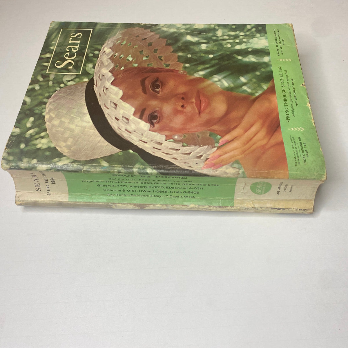 Side view of the 1964 Sears Mr. John Classic Hats Spring - Summer Catalog showcasing the thickness of the magazine and the model on the cover wearing a fashionable hat.
