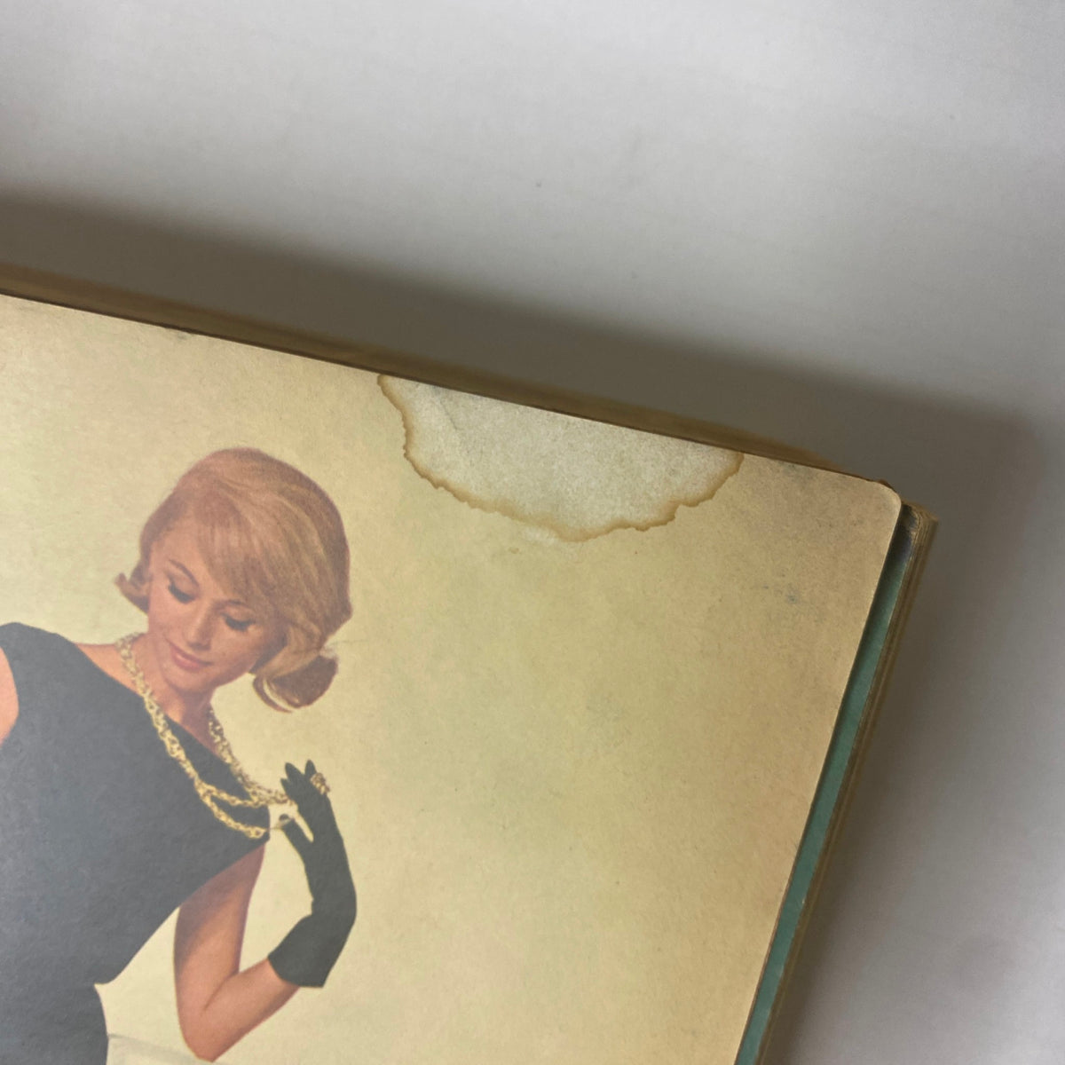 Top edge of the 1964 Sears Mr. John Classic Hats Spring - Summer Catalog showing a vintage fashion scene with a model in a black dress and gloves, indicative of 1960s style.