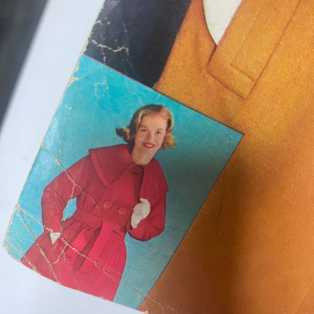 Close-up of a vintage woman's coat advertisement from the 1961 Sears Fall and Winter Catalog, featuring a woman in a stylish red coat against a bright blue background.