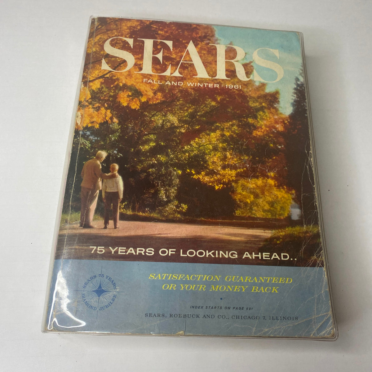 Front cover of the 1961 Sears Fall and Winter Catalog displaying a scenic autumn path with a couple, symbolizing the warmth and nostalgia of mid-century fashion.
