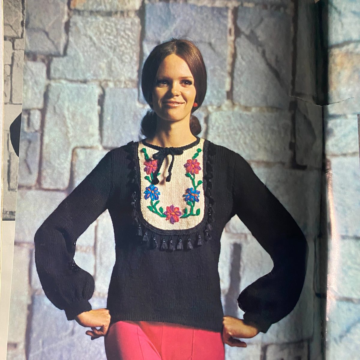 Model wearing a floral-embellished knitted sweater from the 1966 Columbia Minerva Bravo Mexico Knits Pattern Book, set against a textured stone background.