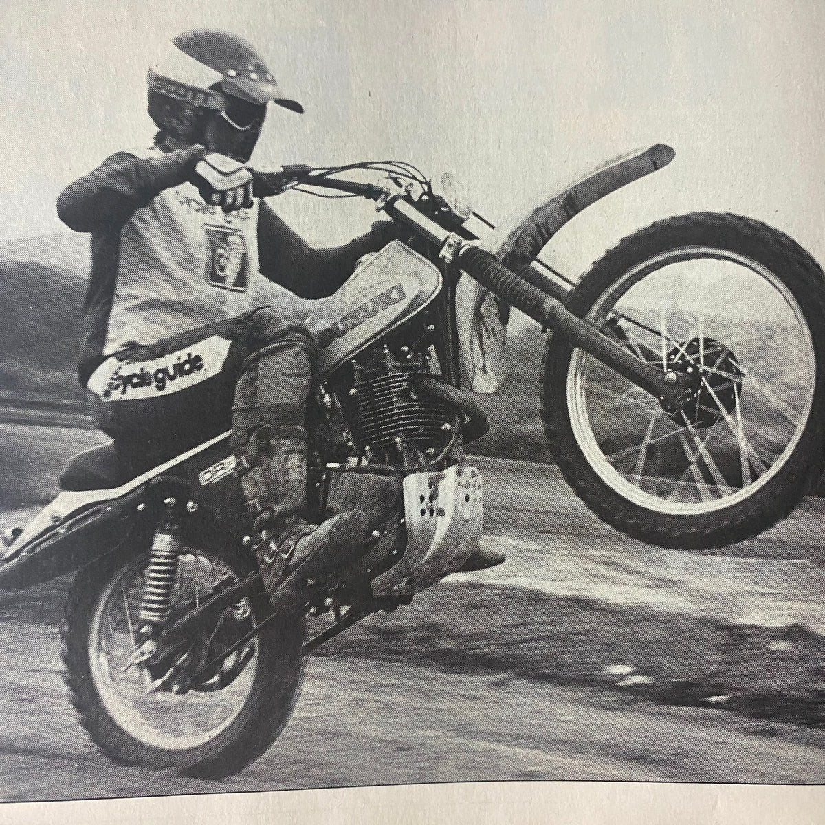 Vintage black and white image of a rider performing a wheelie on a Suzuki dirt bike, featured in Cycle Guide Magazine December 1978.
