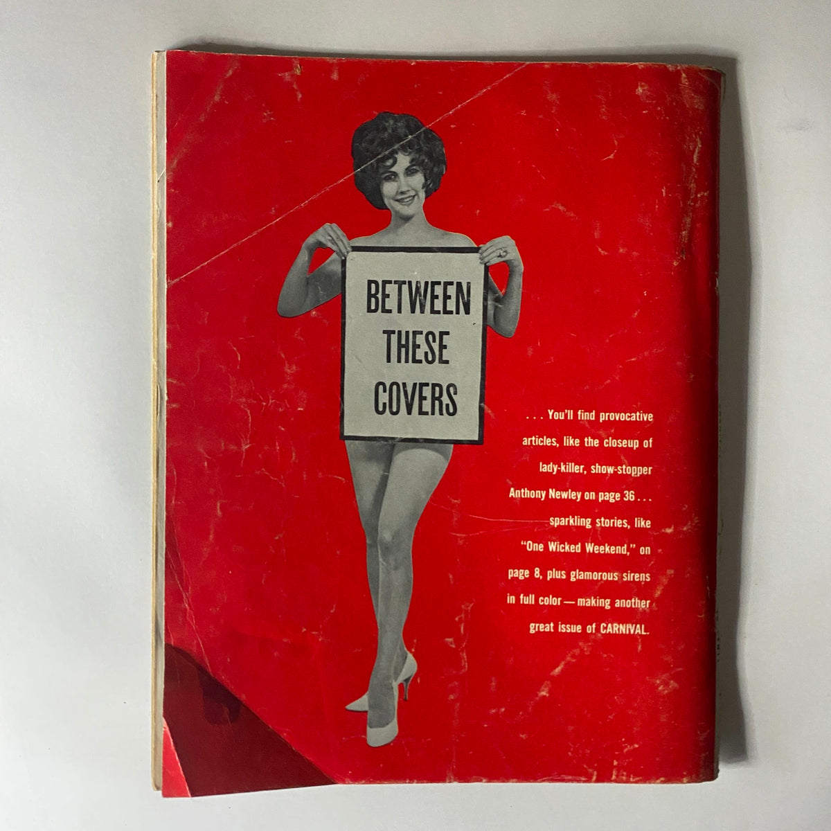 Cover of Carnival Magazine July 1963 Vol 11 No. 1 showcasing a woman holding a sign reading 'BETWEEN THESE COVERS', featuring a vibrant red background, hinting at the provocative articles and stories inside.