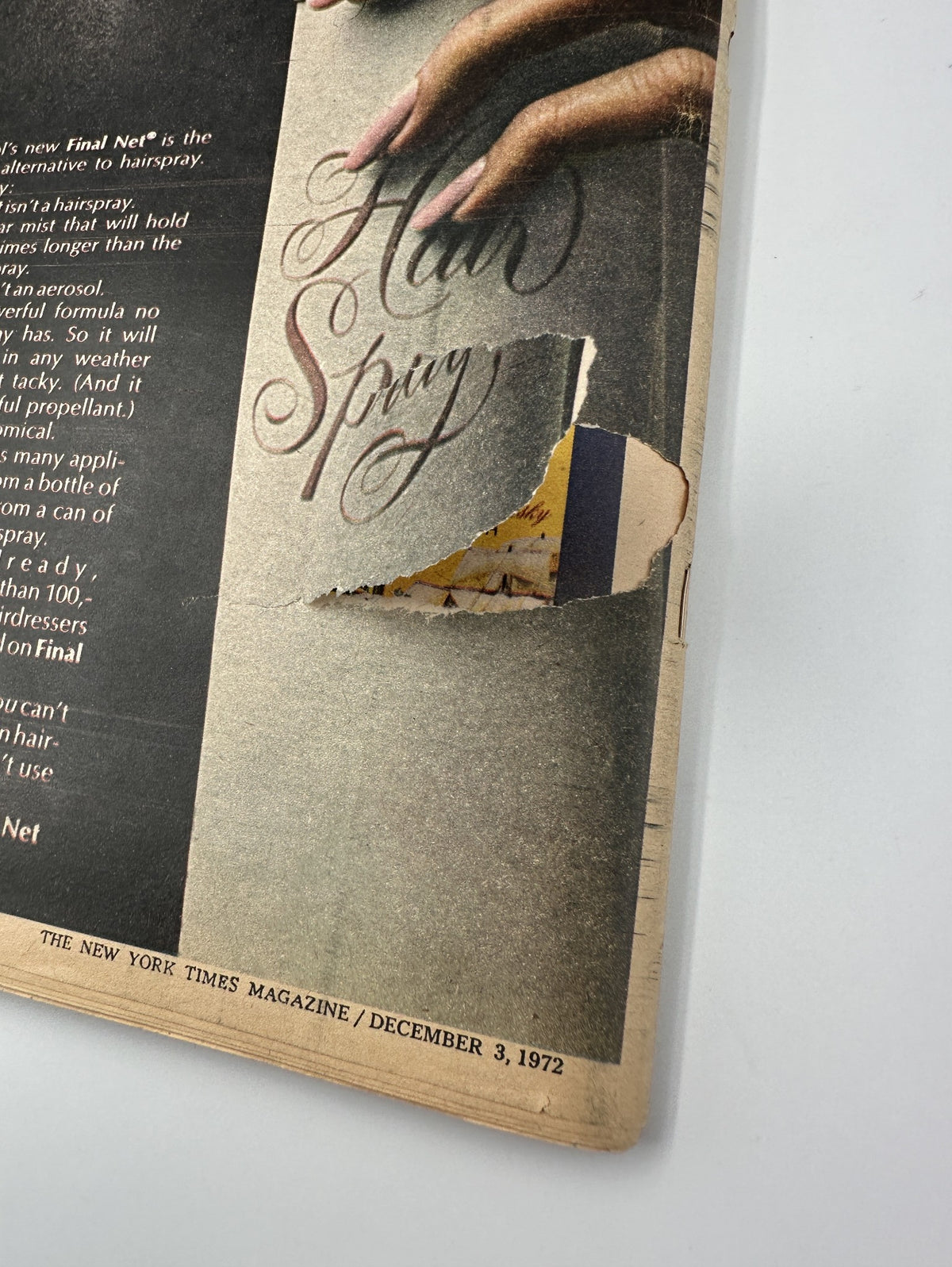 Close-up view of a torn edge on an advertisement page from The New York Times Magazine, December 3, 1972. The page promotes hair products, detailing the benefits of Clarol's Final Net hairspray, showing the text 'Hair Spray'.