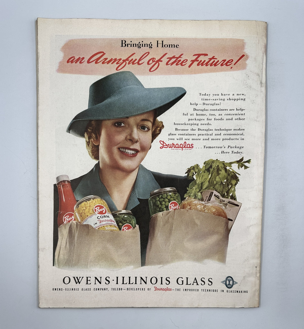 Back cover of Woman's Home Companion Magazine May 1943 illustrating a woman in a teal hat holding grocery bags with food items, promoting the theme 'Bringing Home an Ample of the Future'.