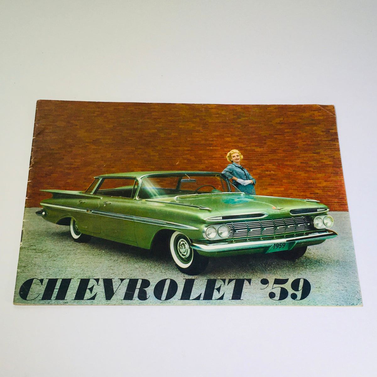 Vintage 1959 Chevrolet Kingswood 4-Door Station Wagon Hardtop Car Catalog Brochure featuring a stylish green vehicle and a woman standing beside it against a brick wall.
