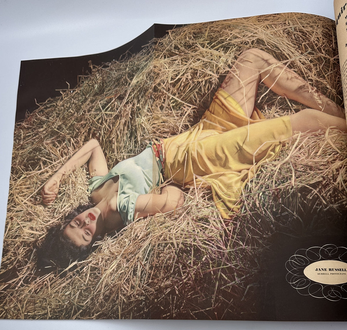 Photograph of actress Jane Russell lying in a hayfield, featured in Esquire Magazine June 1942, displaying a casual and charming summer look.