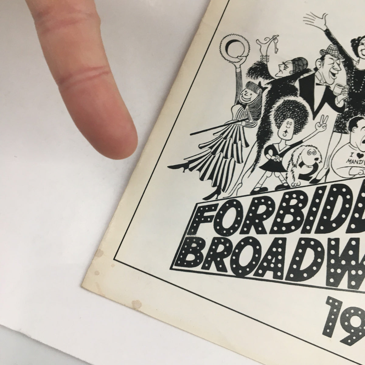 Close-up of the '1990 Playkill Theatre East Forbidden Broadway 90 by Gerard Alessandranini' magazine with a finger pointing at it, highlighting the vintage design and condition.
