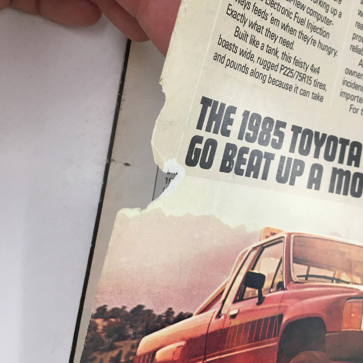 Close-up of the torn edge of the 1985 Toyota 4x4 SR5 magazine advertisement, displaying the caption "Go Beat Up A Mountain," from the Sports Illustrated Magazine December 10 1984 featuring Michael Jordan.